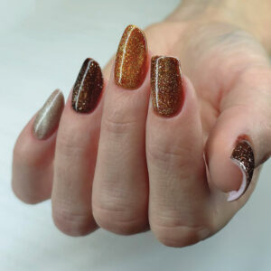 Pose gel aux teintes marron et cuivre pailletées avec ongle accent et détail graphique blanc.