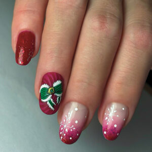 Pose gel rouge dégradé avec nail art hivernal, flocons blancs et décoration 3D effet nœud vert en relief.