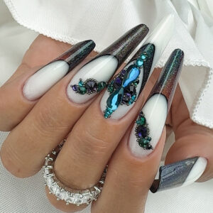 Pose ongulaire forme amande longue avec french blanche, effet chrome sombre et incrustations de strass bleu et vert en relief.