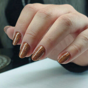 Pose gel courte couleur cuivre pailletée avec finition brillante et forme ovale naturelle.